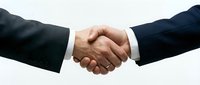 Two businessmen in suits shake hands against a light background, symbolizing agreement, partnership, and successful deal closing.