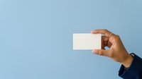 Cropped view of male hand with medium skin tone wearing dark sleeve holding blank white business card against light blue background for branding and corporate identity projects.