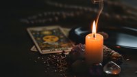 Mystical fortune telling setup with burning candle, tarot cards, crystals and coffee beans creating atmospheric divination scene for spiritual practices.