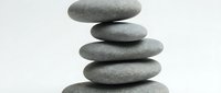Stacked smooth gray stones balanced in zen tower formation against white background, symbolizing harmony, balance, meditation, and wellness for spa and mindfulness design projects.