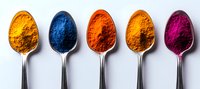 Vibrant colorful spices in silver spoons arranged in row on white background, including turmeric, indigo, paprika, curry and pink pitaya powder for cooking and food coloring.
