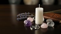 Spiritual wellness setup with white candle, healing crystals, pentagram symbol and dried lavender on wooden surface for meditation and relaxation practices.