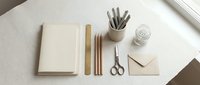 Minimalist workspace flat lay with notebook, wooden pencils, scissors and envelope on neutral beige background for creative projects and stationery design.