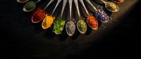 Colorful spices and herbs arranged in wooden spoons on dark background. Culinary ingredients for cooking and seasoning food in circular pattern.