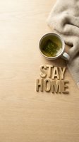 Stay home concept with green tea cup, cozy knit blanket, and wooden letters on light wood surface, top view with copy space.