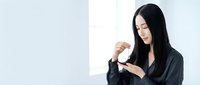 Young Asian businesswoman in black blazer drinking coffee in modern office space with natural lighting for corporate lifestyle concepts.