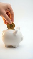Hand inserting golden coin into white ceramic piggy bank on clean background for savings and financial planning concepts.