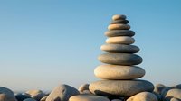 Balanced stone cairn tower on rocky beach against clear blue sky creating zen meditation symbol for mindfulness wellness and spiritual harmony concepts.