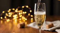 Champagne being poured into a flute glass with golden bokeh lights and cork details in background, suitable for celebration and festive event designs.