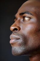 Side profile of young African American male with water droplets on skin against dark background, showing contemplative expression and natural lighting.