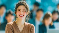 Happy young Asian woman smiling warmly in brown sweater with messy bun hairstyle against blurred crowd background for lifestyle and portrait concepts.