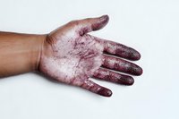 Human palm covered in dark red substance against white background, simulating blood spatter for theatrical or Halloween makeup effects, dramatic crime scene staging.