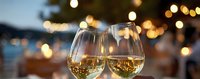Two glasses of white wine toasting against blurred evening background with bokeh lights and waterfront view.