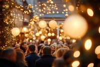 Festive crowd walking through illuminated Christmas market with glowing paper lanterns and string lights creating magical bokeh atmosphere at dusk.