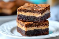 Decadent layered chocolate brownies with creamy peanut butter filling stacked on white plate, showing rich fudgy texture and moist interior in close-up view.