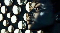 Profile of African woman with black face paint against illuminated circular background, dramatic lighting creating artistic contrast for fashion editorial.