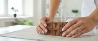 Person arranging wooden blocks with business icons on white desk in bright office environment for strategic planning and organizational concepts.