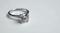 Elegant diamond engagement ring with round brilliant cut stone and platinum band on neutral gray background. Symbolizes love and commitment.