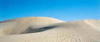 Vast sand dunes with rippled texture under clear blue sky, showcasing desert landscape and natural geological formations for travel and nature projects.