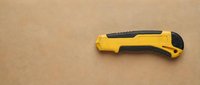 Yellow utility knife with black grip on brown cardboard background for construction and crafts projects.