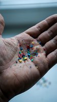 Hands holding colorful microplastic particles collected from ocean water showing marine pollution and environmental contamination impact on ecosystems.