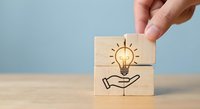 Hand placing wooden blocks with lightbulb and hand icons representing innovation, creativity, and idea development for business solutions.