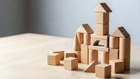 Wooden building blocks arranged as miniature houses and towers on light surface, creative construction play for children development and learning.