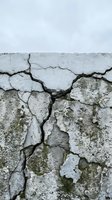 Weathered concrete wall with deep cracks and peeling paint showing age and deterioration against cloudy sky for construction and repair concepts.