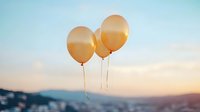 Orange balloons floating against pastel sunset sky with soft clouds and mountain silhouette in background, creating dreamy atmospheric mood for celebration and freedom concepts.