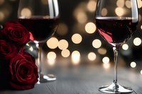 Red wine glasses with romantic bokeh lights and deep red roses create intimate Valentine's Day or anniversary ambiance on dark background.