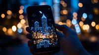 Smartphone screen displaying illuminated city skyline with glowing skyscrapers against dark background, surrounded by blurred golden bokeh lights creating magical atmosphere.