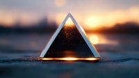 Glowing triangular prism on reflective surface with sunset bokeh background creates mystical atmosphere, orange light streaming through geometric shape in dark setting.