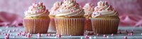 Vanilla cupcakes topped with pink and white swirled buttercream frosting, decorated with heart-shaped sprinkles on pink background, romantic dessert panorama.