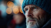 Thoughtful senior man with gray beard wearing knit hat against bokeh lights background. Portrait captures wisdom and contemplation in urban evening setting.