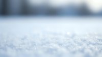 Close-up macro view of fresh white snow crystals and snowflakes on ground surface with soft blurred winter background creating peaceful seasonal atmosphere.