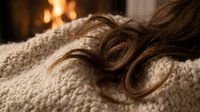 Cozy winter evening with wavy brown hair on knitted blanket by warm fireplace creating relaxing hygge atmosphere for wellness and self-care moments.