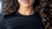 Young mixed race woman with curly dark hair wearing black top, cropped portrait showing gentle smile and natural makeup, soft lighting creates professional look.