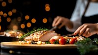 Roasted meat with herbs and vegetables on wooden board, chef preparing festive dinner in restaurant kitchen with warm bokeh lights background.
