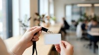 Employee holding blank ID badge card in modern office workplace environment with colleagues in background.