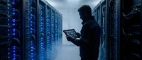 IT technician monitoring server room with tablet computer in modern data center with blue LED lights and network equipment racks for cloud computing operations.