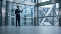 Professional businessman in dark suit presenting digital interface with network icons in modern glass office building with steel framework architecture.