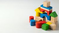 Colorful wooden building blocks and geometric shapes scattered on white background for educational play and child development activities.