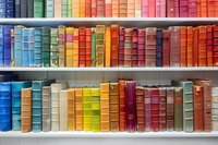 Colorful vintage books arranged by spectrum colors on white library shelves, creating rainbow pattern of spines for home decor or bookstore display.