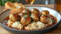 Homemade meatballs with herbs served over rice in rich tomato sauce on dark plate. Comfort food dinner meal with bread and wine in background.