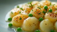 Tender baby potatoes garnished with fresh herbs, black pepper and green peas on white plate, macro food photography with soft focus and natural lighting.