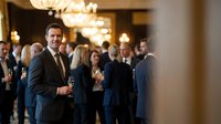 Confident businessman in elegant suit holding champagne glass at upscale corporate networking event with colleagues in luxurious venue with chandeliers.