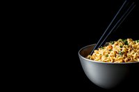 Asian instant ramen noodles in bowl with chopsticks on black background for food photography and culinary design projects.
