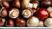 Fresh brown and white mushrooms with red cherry tomato in macro view, showing texture and natural patterns of raw organic produce for cooking background.