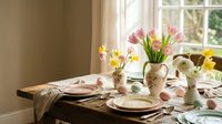 Spring table setting with pink tulips and daffodils in ceramic vases by sunny window. Elegant dining room decor with natural light and fresh flowers.