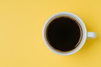 White ceramic cup filled with black coffee on vibrant yellow background, top view with copy space. Minimalist composition for cafe menu or coffee break concept.